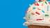 Close-up of an ice cream cone topped with vanilla ice cream and colorful sprinkles against a blue background. - Olive Oil Times