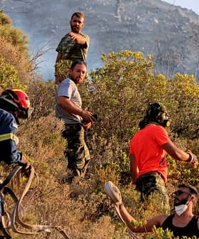 Firefighters and volunteers working together to manage a wildfire in a hilly area with vegetation. - Olive Oil Times