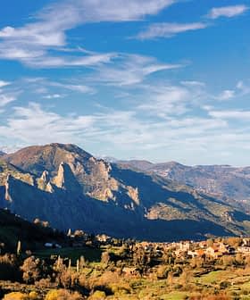 Scenic view of mountains with a small village nestled in the valley under a blue sky. - Olive Oil Times
