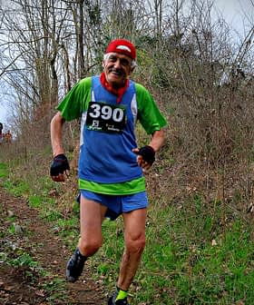 Two trail runners participating in a race on a wooded path, one wearing a green and blue outfit with a race number. - Olive Oil Times