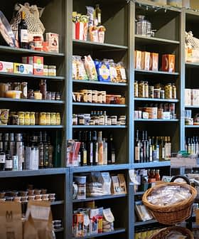 Wooden shelves filled with jars, bottles, and packaged food items in a grocery store. - Olive Oil Times
