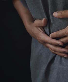 Individual wearing a gray shirt, holding their stomach with both hands, indicating discomfort. - Olive Oil Times
