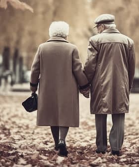 An elderly couple holding hands while walking through a park covered in autumn leaves. - Olive Oil Times