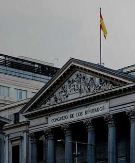 The Congreso de los Diputados building in Spain with a statue in front and a flag on top. - Olive Oil Times