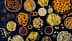 An assortment of snack foods including chips, pretzels, and popcorn arranged in bowls on a dark surface. - Olive Oil Times