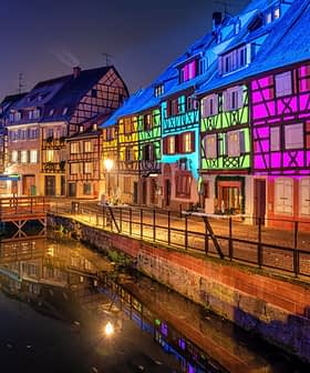 Row of half-timbered houses illuminated in various colors along a canal at night. - Olive Oil Times