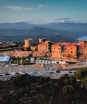 Aerial view of a historic castle surrounded by mountains and greenery. - Olive Oil Times