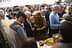 A group of people gathered around a table discussing various items at an outdoor event. - Olive Oil Times