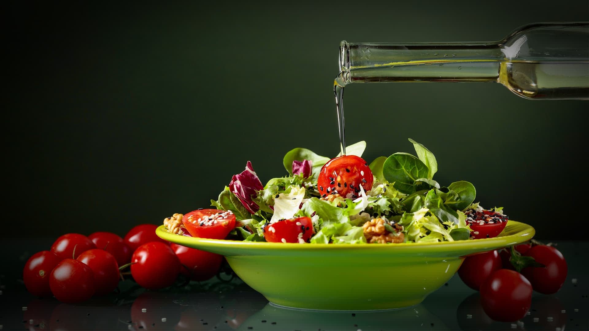 A bowl of mixed salad with cherry tomatoes and olive oil being poured over it. - Olive Oil Times