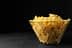 A clear glass bowl filled with yellow tortilla chips on a dark surface. - Olive Oil Times