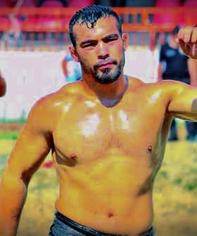 A male wrestler with a muscular build, wearing traditional oil wrestling attire, standing in a field. - Olive Oil Times