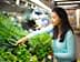 Woman with long black hair selecting fresh greens from a grocery store display. - Olive Oil Times