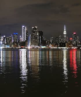 Night view of the New York City skyline with illuminated buildings reflecting on the water. - Olive Oil Times