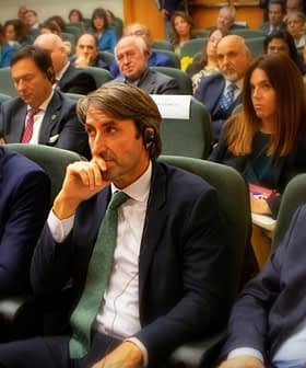 A group of individuals seated in a conference setting, some wearing headphones and engaged in discussion. - Olive Oil Times