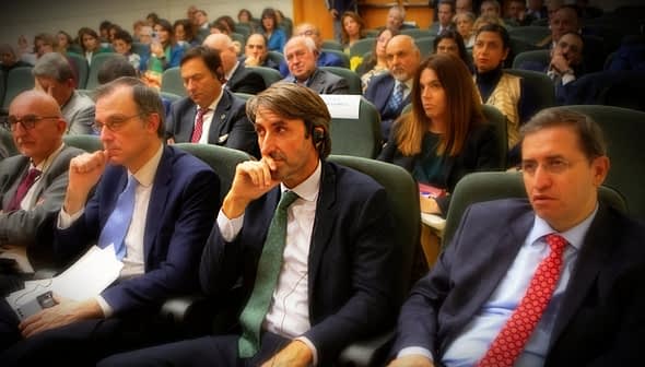 A group of individuals seated in a conference setting, some wearing headphones and engaged in discussion. - Olive Oil Times