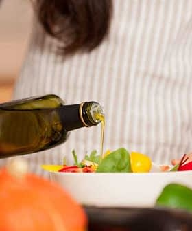 Individual pouring olive oil from a bottle into a salad bowl filled with vegetables. - Olive Oil Times