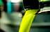 Stream of bright green olive oil pouring from a metal spout into a container. - Olive Oil Times