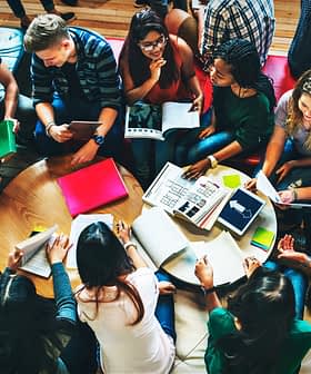 A diverse group of individuals gathered around a table, engaged in discussion with notebooks and materials. - Olive Oil Times