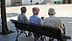 Three elderly men sitting on a bench, viewed from behind, in a public square. - Olive Oil Times