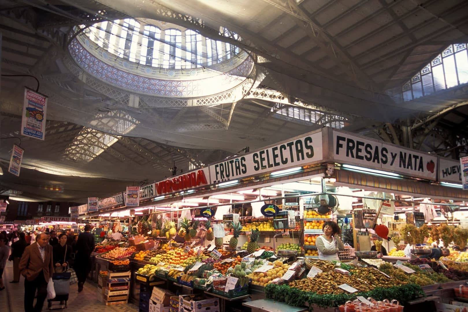 Market stall displaying a variety of fruits and vegetables under a large skylight. - Olive Oil Times