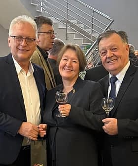 Three individuals standing together, each holding a glass, in a gathering or event setting. - Olive Oil Times