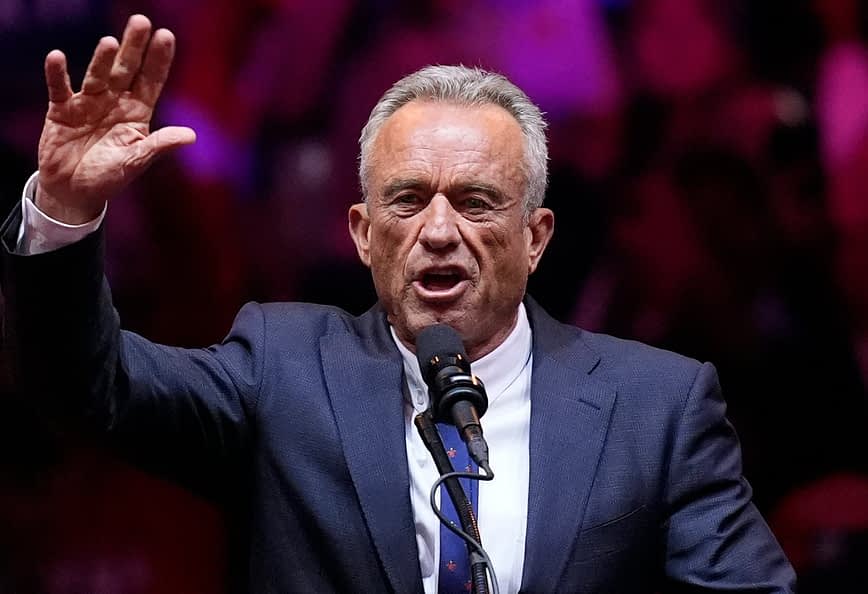 A man in a suit speaking passionately into a microphone while raising his hand. - Olive Oil Times