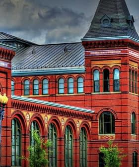Historic red brick building featuring multiple towers and arched windows against a cloudy sky. - Olive Oil Times