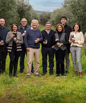 Group of twelve individuals standing in an olive grove, each holding a bottle of olive oil. - Olive Oil Times