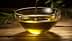 A clear glass bowl filled with olive oil, with olive branches placed nearby on a wooden surface. - Olive Oil Times