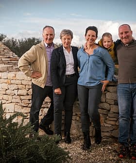 A group of six people standing together near a stone structure with a circular top. - Olive Oil Times