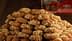 A large stack of honey-dipped cookies topped with crushed nuts on a wooden surface. - Olive Oil Times