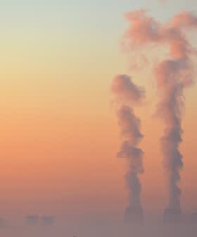 Three smoke stacks emitting vapor into the sky during sunrise with a gradient of colors. - Olive Oil Times