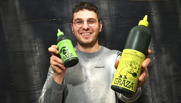 Person holding two bottles of Grazia extra virgin olive oil, one large and one small, both with green labels. - Olive Oil Times