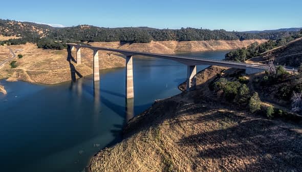 A bridge spanning over a body of water with supporting pillars and surrounding landscape. - Olive Oil Times