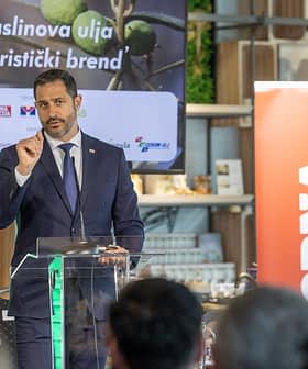 A man in a suit speaking at a podium during an event about olive oil as a tourist brand. - Olive Oil Times
