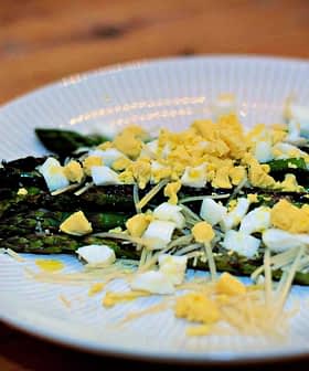 Plate of cooked asparagus topped with chopped egg and grated cheese. - Olive Oil Times