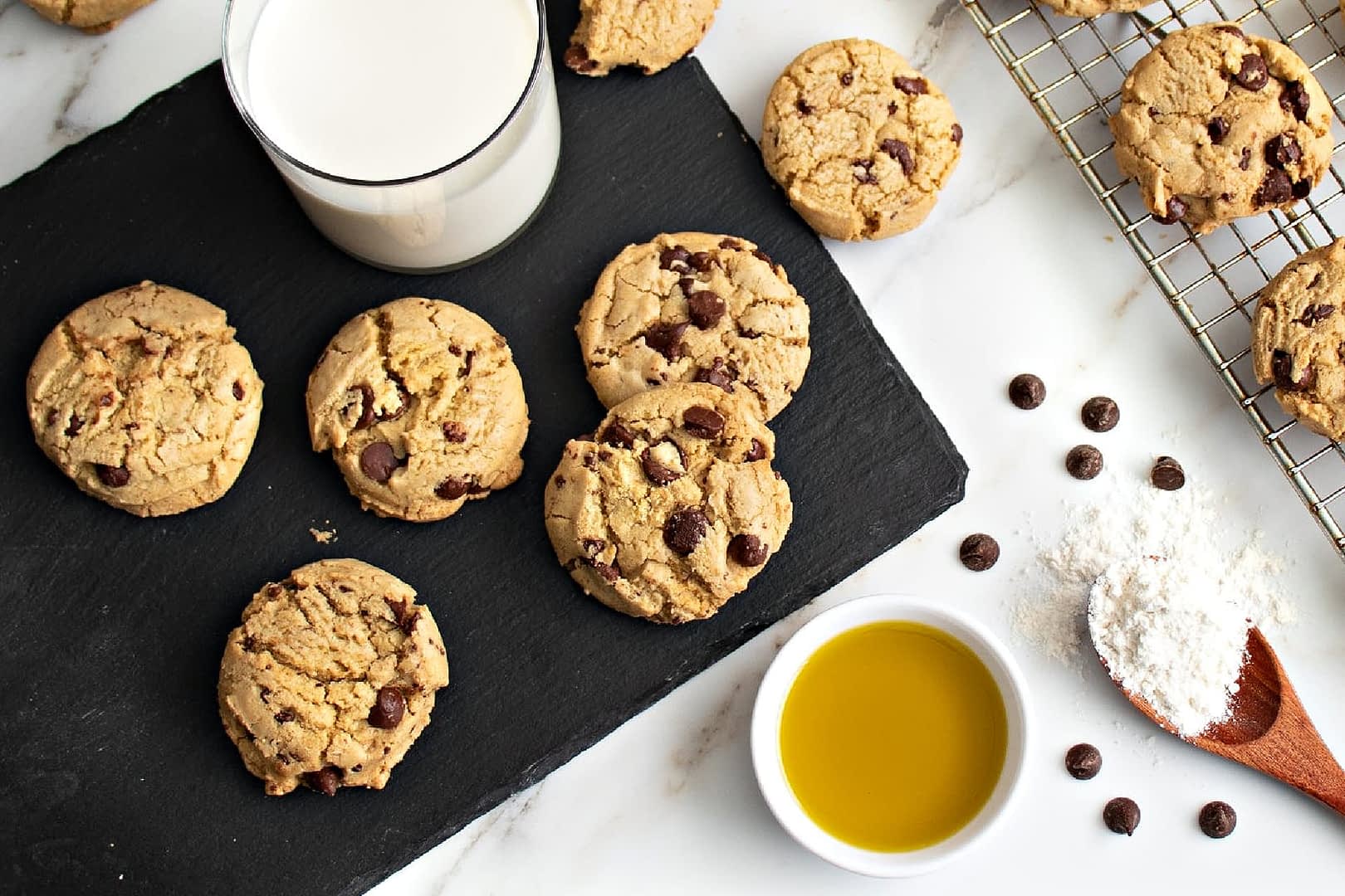 Plate of chocolate chip cookies next to a glass of milk and a bowl of olive oil. - Olive Oil Times