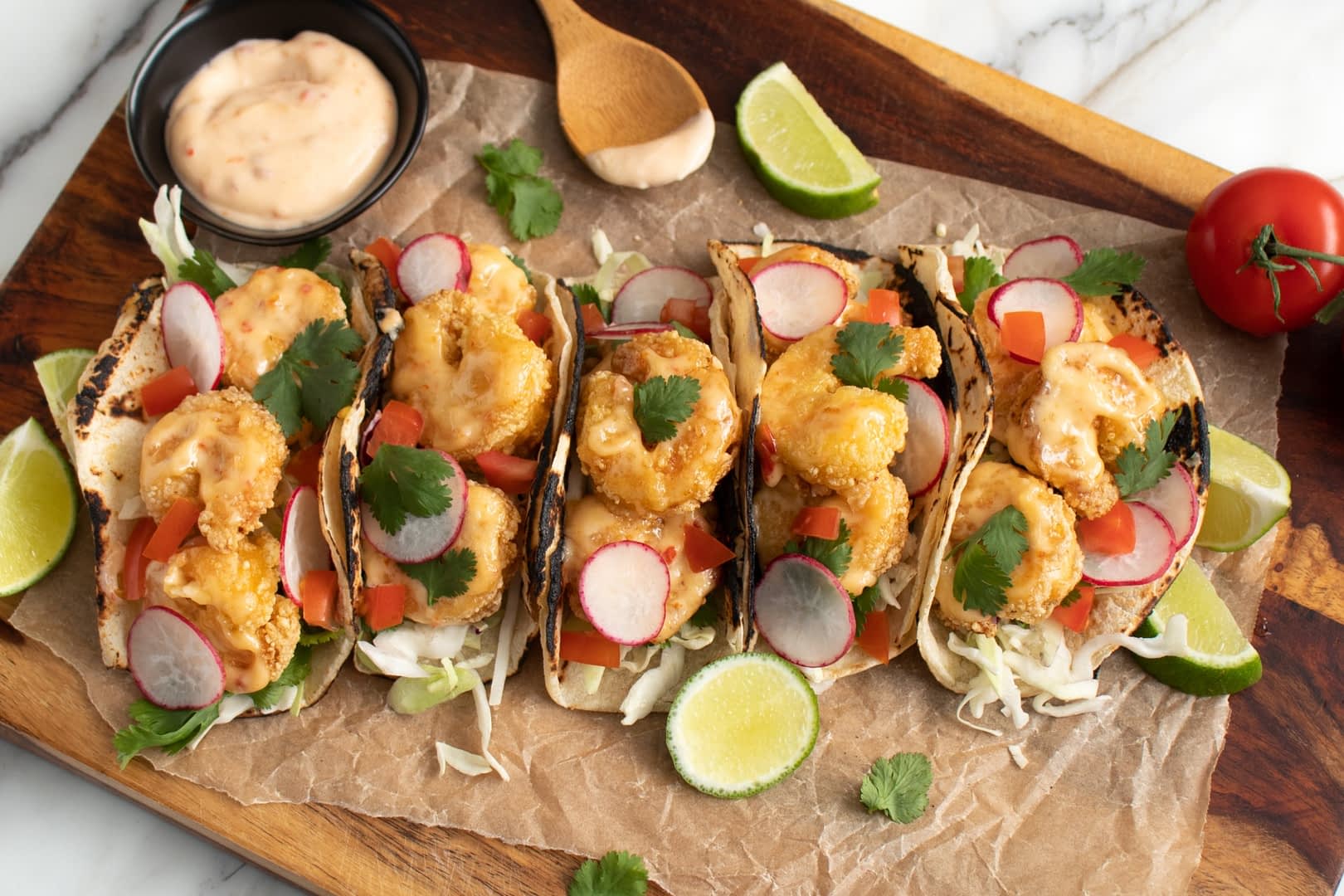 Five shrimp tacos topped with vegetables and sauce on a wooden serving board. - Olive Oil Times