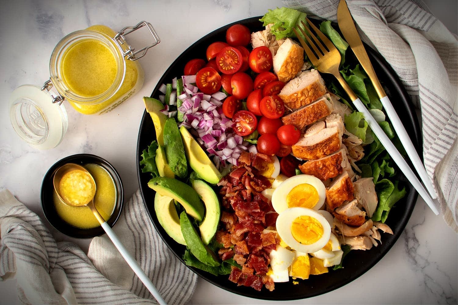 A colorful salad featuring grilled chicken, avocado, cherry tomatoes, and hard-boiled eggs on a black plate. - Olive Oil Times