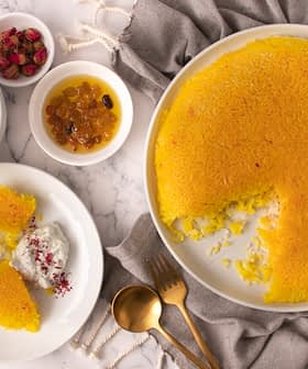 A round saffron rice dessert with a portion removed, served with yogurt and dried fruits. - Olive Oil Times
