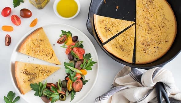 Sliced chickpea flour flatbread served with a fresh salad of tomatoes and greens. - Olive Oil Times
