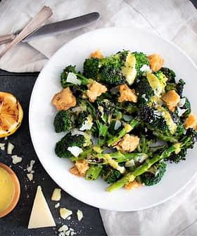 Plate of broccoli and asparagus salad with lemon, cheese, and croutons on a table. - Olive Oil Times