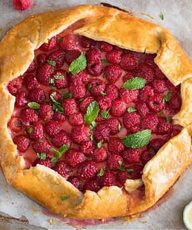 A raspberry galette topped with fresh mint leaves and lime slices on a baking sheet. - Olive Oil Times
