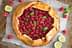 A raspberry galette topped with fresh mint leaves and lime slices on a baking sheet. - Olive Oil Times