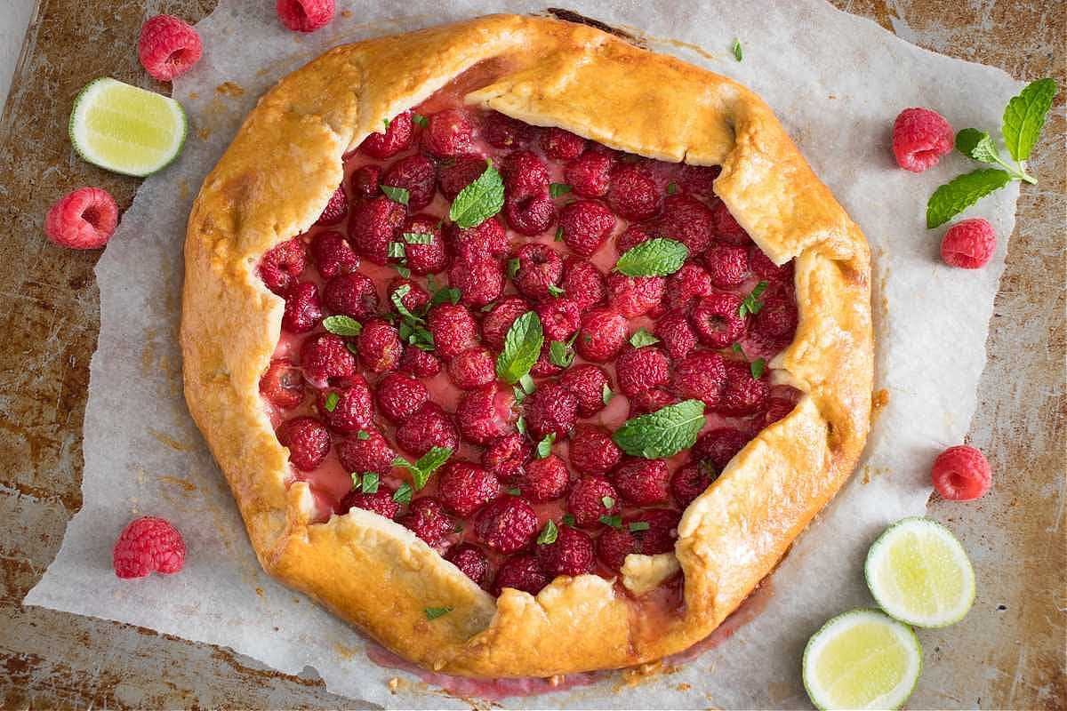 A raspberry galette topped with fresh mint leaves and lime slices on a baking sheet. - Olive Oil Times