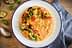 Bowl of creamy risotto topped with grilled vegetables and cherry tomatoes on a wooden table. - Olive Oil Times