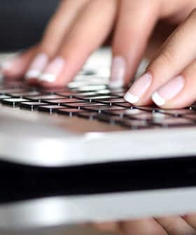 Close-up of hands typing on a laptop keyboard with a reflective surface. - Olive Oil Times
