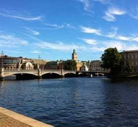 View of a bridge over water in Stockholm with buildings and trees in the background. - Olive Oil Times
