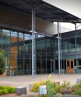 Entrance of a modern building featuring large glass windows and a metal roof structure. - Olive Oil Times
