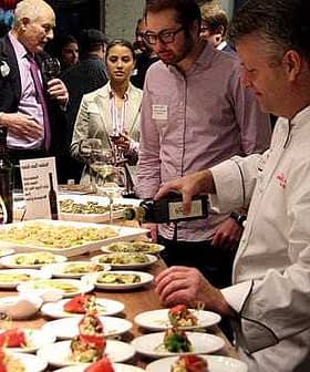 Chef pouring olive oil over a plate of food at a culinary event with attendees observing. - Olive Oil Times